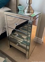 Front and side angled view of mirrored glass night stand with beveled edges and three drawers showing crystal knobs