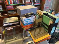 Photo showing stacked office supplies including paper reams, folders, binders, and organizers.