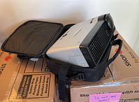 Side view of projector inside padded soft carrying case, showing form-fitting design and shoulder strap.