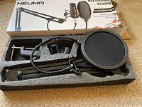 Photo of Neuma recording studio accessory set in original packaging, showing microphone stand and pop filter inside molded foam case.
