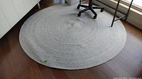 Full view of large round braided rug on wooden floor with office chair on top