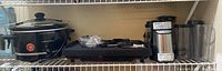 Photo of slow cooker, double burner electric skillet, Cuisinart blender with large pitcher, and blender base on a shelf