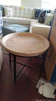 Side view of the round wood top and metal base end table next to a white sofa and ottoman.