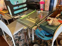 Oblique view of full table showing clutter removed: clear glass top on silver tubular frame, extension rails visible.