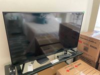 Front view of TV on glass table with two remotes and storage boxes in background