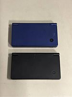 Top closed view of both Nintendo DSi consoles stacked, showing black and blue colors.