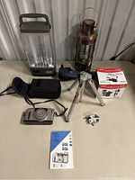 Photo showing Coleman camping lantern, vintage copper lantern, Minolta mini tripod, Canon Prima Zoom 70 camera with case, camera accessory box, and Canon camera manual placed on a table.