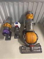 Full lot showing Dyson upright vacuum cleaner and two separate dust bin and motor parts on a table against a radiator.