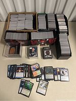 Overview of multiple boxes filled with loose trading cards, loose Magic cards fanned out, a hockey card in a toploader and a sealed Warhammer sleeves box