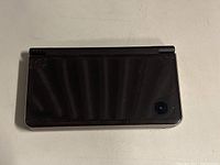 Closed Nintendo DS XL showing top lid with camera lens in the upper right corner.