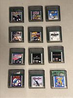Nintendo Gameboy Color handheld console and 12 game cartridges laid out in a grid on a flat surface.