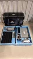 Nintendo Wii black console set laid out in original box including remote, power adapter, AV cables, and manuals.