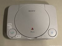 Top view of the white Sony PSone PlayStation console showing the PSone logo, power and reset buttons, and condition stickers.