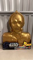 Front view of the gold plastic molded Star Wars C-3PO electronic talking carry case with packaging base and branding.