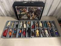 Two open gray trays of Star Wars figures laid out beneath black Kenner case lid; left and right trays visible