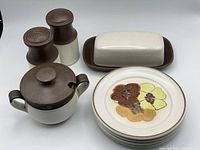 Four side plates with floral design, along with covered butter dish, covered sugar bowl, and salt and pepper shakers shown together on white background.