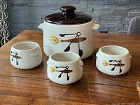Large covered bean pot with 3 small matching bean bowls on wooden table, design in black and yellow on white ceramic body with dark brown lid.