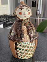 Front and side view of 1960's folk art babushka jug, showing full body and hand-painted details including clothing patterns and facial features.