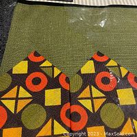 Close-up of the placemats and napkins showing woven green background and colorful geometric shapes of orange, yellow, brown and green.