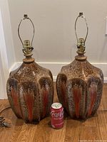 Two brown and orange ceramic lamps with brass harps and electrical cords shown with soda can for size reference