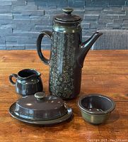 Full set of Franciscan Madeira coffee pot, creamer, sugar bowl, covered butter dish on wooden table with stone wall background.