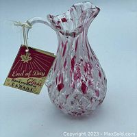 Full view of the cranberry and white hand crafted glass pitcher showing the diamond textured base and ruffled top with attached original tag.