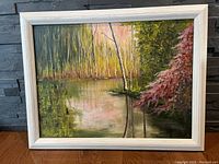 Frontal view of the framed impasto painting depicting a forest with water reflection in a white frame