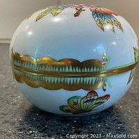 Side view showing gold scalloped band around middle along with floral motifs on white porcelain base.