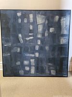 Frontal photo of the large, square, framed abstract painting showing geometric blocks and brush strokes in shades of blue and grey with white accents.
