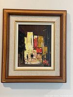 Framed mid century oil painting with street scene dominated by yellow and red building shapes and silhouetted figures.