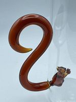 Close-up photo of the curled amber glass handle shaped like a squirrel's tail attached to the glass pitcher.