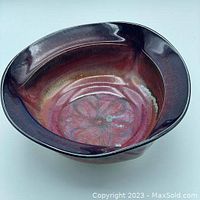 Oblique view of the porcelain bowl showing its irregular rim and glossy red-purple glaze.