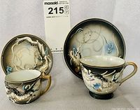 Two embossed demi teacups and matching saucers with dragon design, all arranged for clear view of theme and condition.