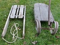 Two antique wooden children's sleighs on grass, showing top and side views with rope and metal runners
