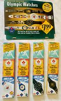 Four new in box Official Olympic Watches from 1996 Atlanta Games, showing all watches in original packaging with colorful Olympic-themed imagery and pricing flyer.