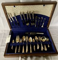 Open wooden presentation box showing the full set of silverware, displaying various spoons, forks, knives and serving utensils arranged in blue velvet lining.