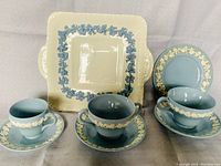 Photo showing the entire tea set with 3 blue cups and saucers, and one cream colored square plate with blue grape vine pattern.