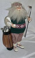 Front view of the vintage golfer doll holding a golf club and standing next to a golf bag with clubs