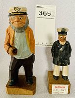 Two hand carved wooden fisherman figurines displayed side by side, showing size and detail differences.