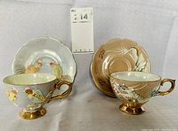 Two sets of hand painted Japanese embossed teacups with matching saucers, one set with fighting rooster design and the other with dragon design, photographed side by side.
