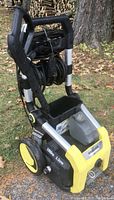Side view of Karcher electric power pressure washer showing yellow wheels, detergent tank, handle, and coiled hose.