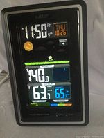 Photo of the front view of the La Crosse wireless weather station showing time 11:58 AM, date Thu 10/26, outdoor temperature 140°F (likely an error or sensor disconnected), indoor temperature 63°F, and humidity 65%. The display shows sun icon for weather and pressure trend.