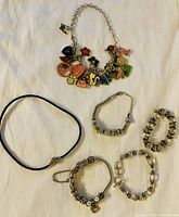 Photo showing six pieces of ladies charm jewelry including colourful Pandora charm bracelet and other silver-tone charm bracelets.
