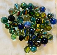 Top-down photo showing approximately 50 assorted vintage glass marbles with various internal swirl colors and patterns.
