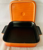 Top view of square ceramic baking dish with orange lid and black interior.