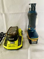 Ryobi battery inserted in yellow 30-minute charger alongside the rotary cutter tool standing upright.