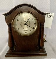 Front view of the wood cased mantle clock showing clock face with hour and seconds displayed, wood case with columns on either side.