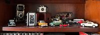 Wide view of antique cameras and die cast cars displayed on wood shelf