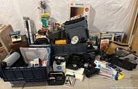 Wide view showing large assortment of cameras, flashes, bags, and accessories stacked in tubs and cases on floor.