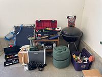 Full view of the lot including grill, sleeping bags, toolboxes filled with tools, portable lantern, and miscellaneous items gathered on floor